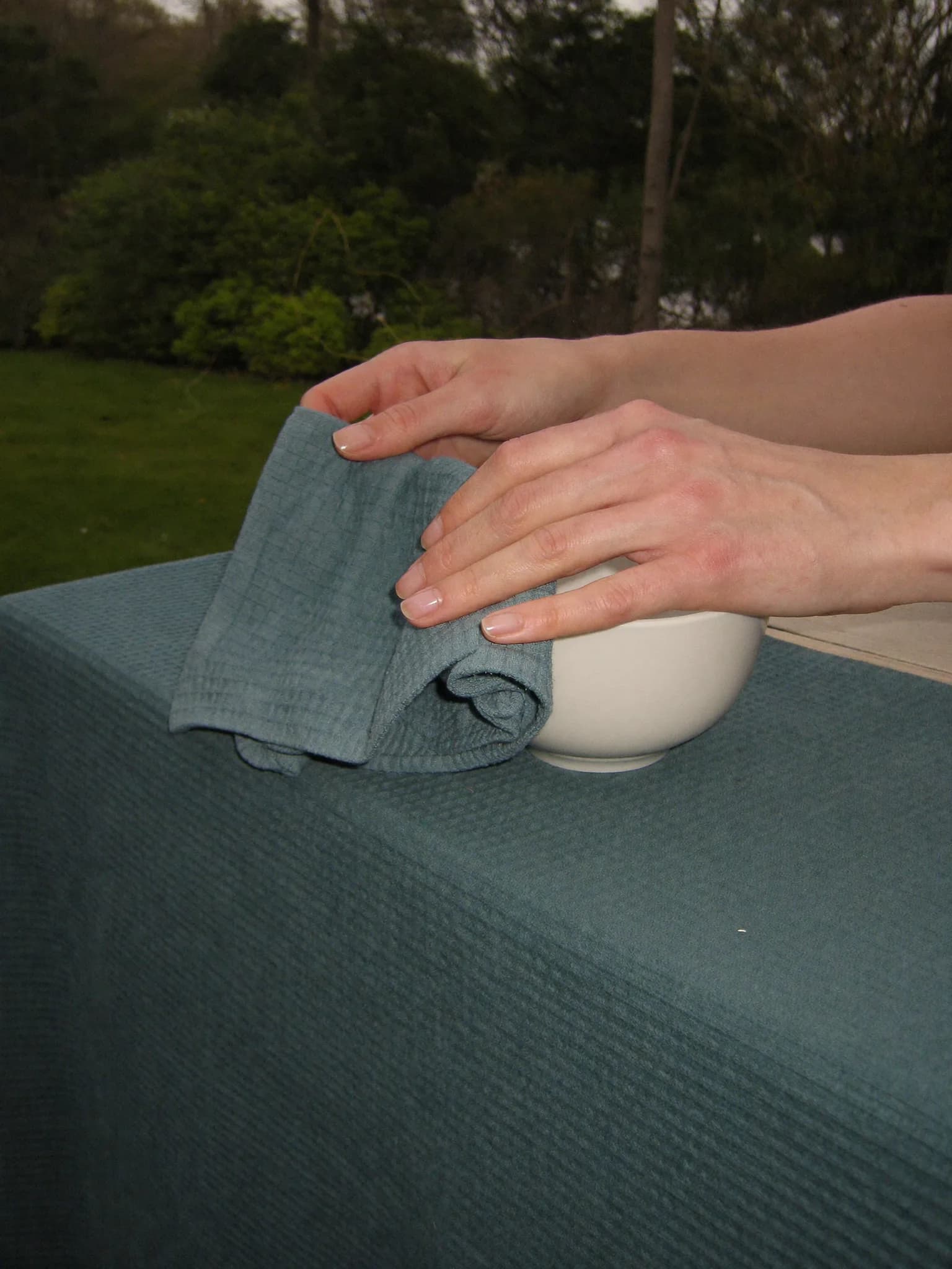 Hands drying a white bowl with a teal waffle towel