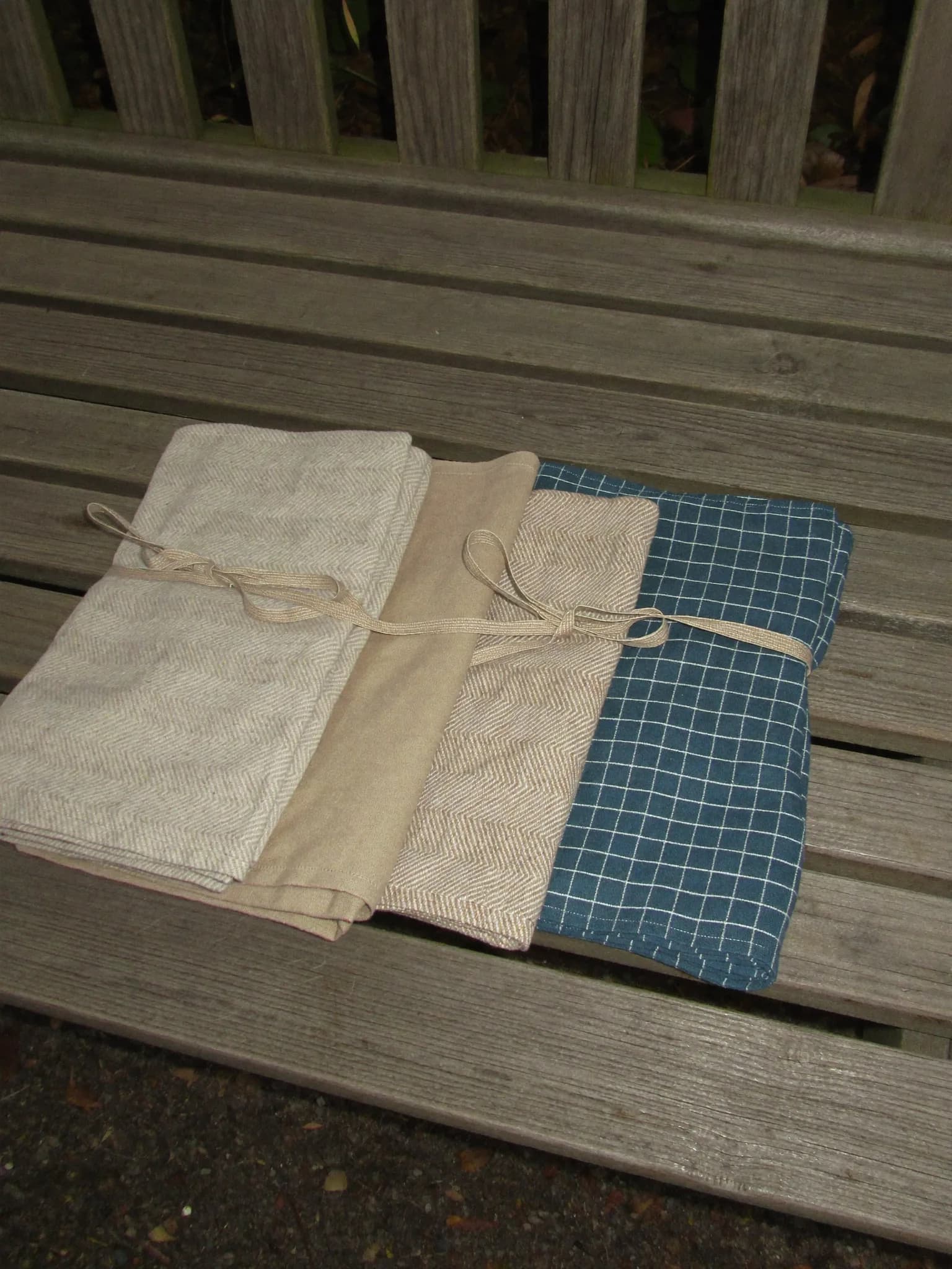 Mixed Set of 4 in Oat, Natural, Sand, Teal, folded on a wooden garden bench
